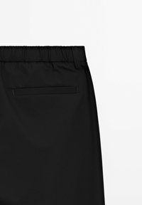 Pantaloni sportivi neri con vita elastica, dotati di una tasca posteriore con filetto singolo e una texture liscia e opaca.