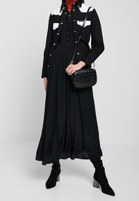 Černé šaty se bílými akcenty, až po kotníky a s volnou látkou. V kombinaci s černou kabelkou se cvočky a černými vysokými botami ke kolenům.