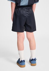 Svarta idrottsshorts med ett strukturerat, randigt mönster, elastisk midja, i kombination med vita strumpor och blå sneakers.