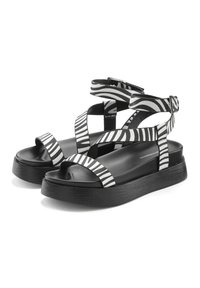 Black and white striped sandals with a thick sole, open-toe design, cross straps, and adjustable ankle straps. Made from synthetic materials.