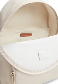 Κρεμ χρώματος σακίδιο με απαλό ύφασμα, κλείσιμο με φερμουάρ και λευκό καπάκι. Το εσωτερικό διαθέτει ταμπά δερμάτινη ετικέτα και ανοιχτό στρίφωμα.