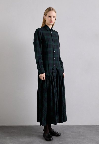 Lang, knappet kjole lavet af mørkegrøn og sort ternet stof. Har en samlet talje og lange ærmer. Matcher med sorte loafers.