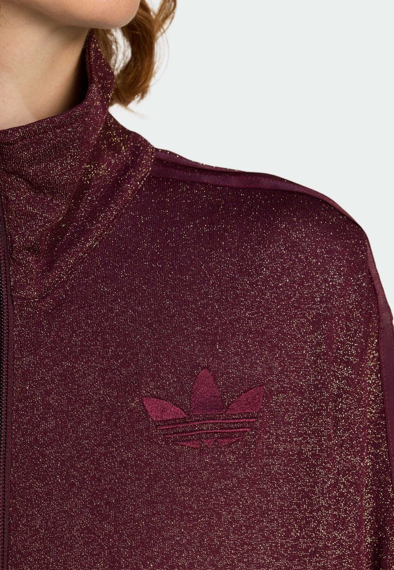 Bordeaux ritsjack met een hoge kraag, glanzende textuur en een bordeaux geborduurd logo op de bovenste linkerzijde.