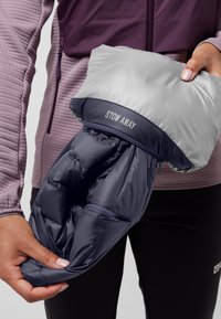 Veste pliable avec un extérieur gris et une doublure bleu marine foncé. Dispose d'une poche zippée. L'étiquette "STOW AWAY" est visible sur le col.