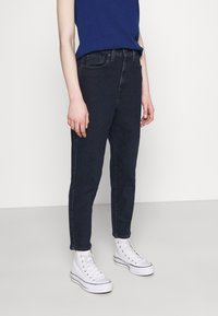 Mörkblå jeans med slim fit, som har framfickor och diskret sömnad. Kombination med vita högskurna sneakers.