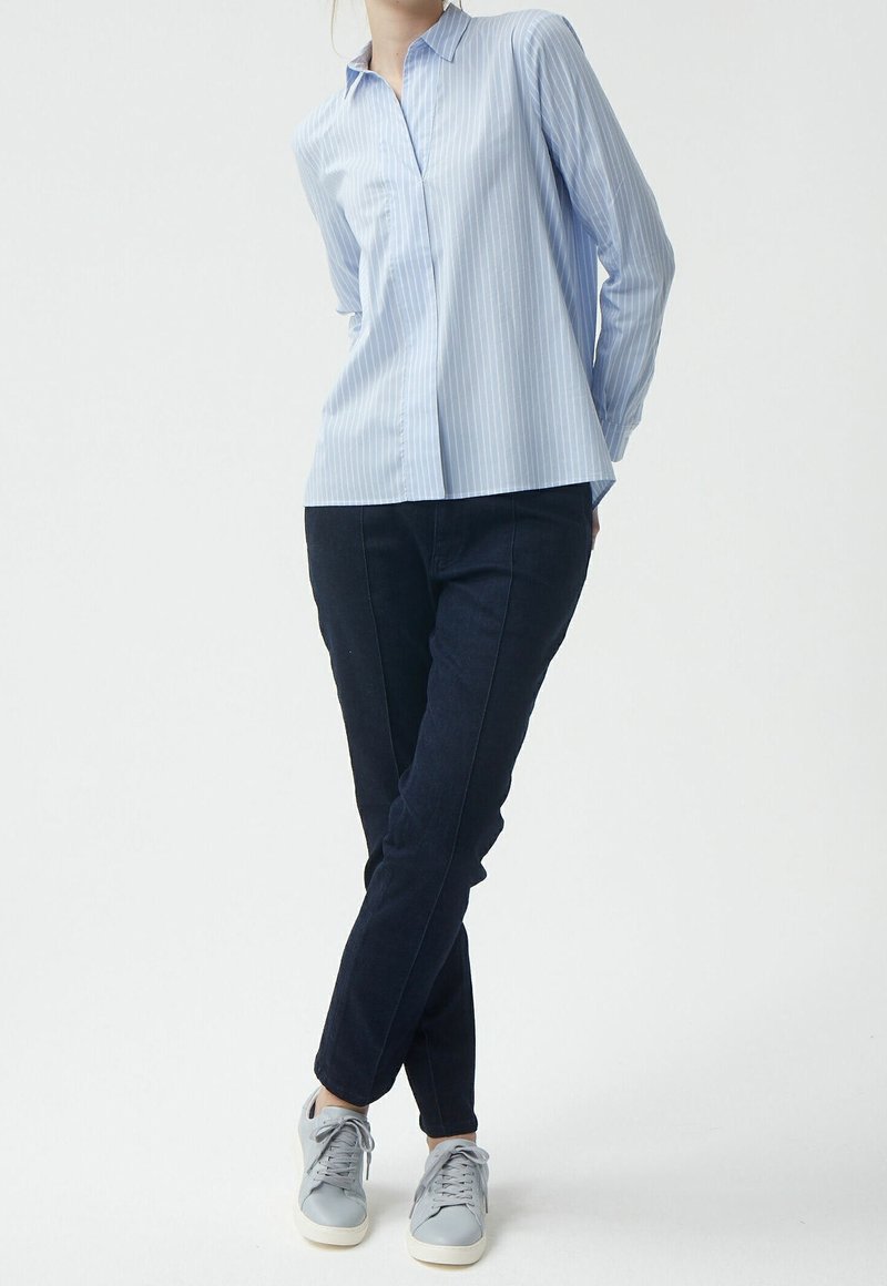 Chemise rayée bleu clair avec un col, associée à un pantalon slim noir et des baskets grises claires. Style décontracté et moderne.