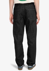 Jean en denim noir avec une coupe ample, dotés de deux poches arrière, de coutures visibles et d'un ourlet retroussé. Porté avec un t-shirt de couleur claire.