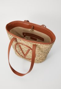 Geflochtene Strohtasche mit braunen Ledergriffen und Akzenten. Innenausstattung mit beigem Futter und einem Reißverschlussfach, sowie einem V-förmigen Detail an der Vorderseite.