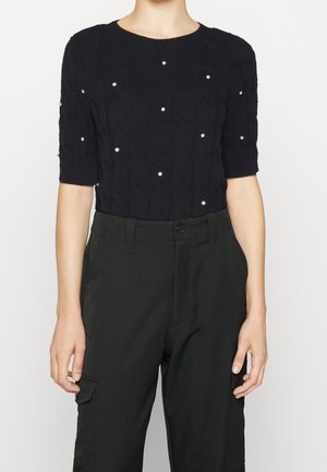 Zwart gebreid top met korte mouwen, versierd met parels en pailletten, gecombineerd met zwarte hoge taille broek met voorzakken.