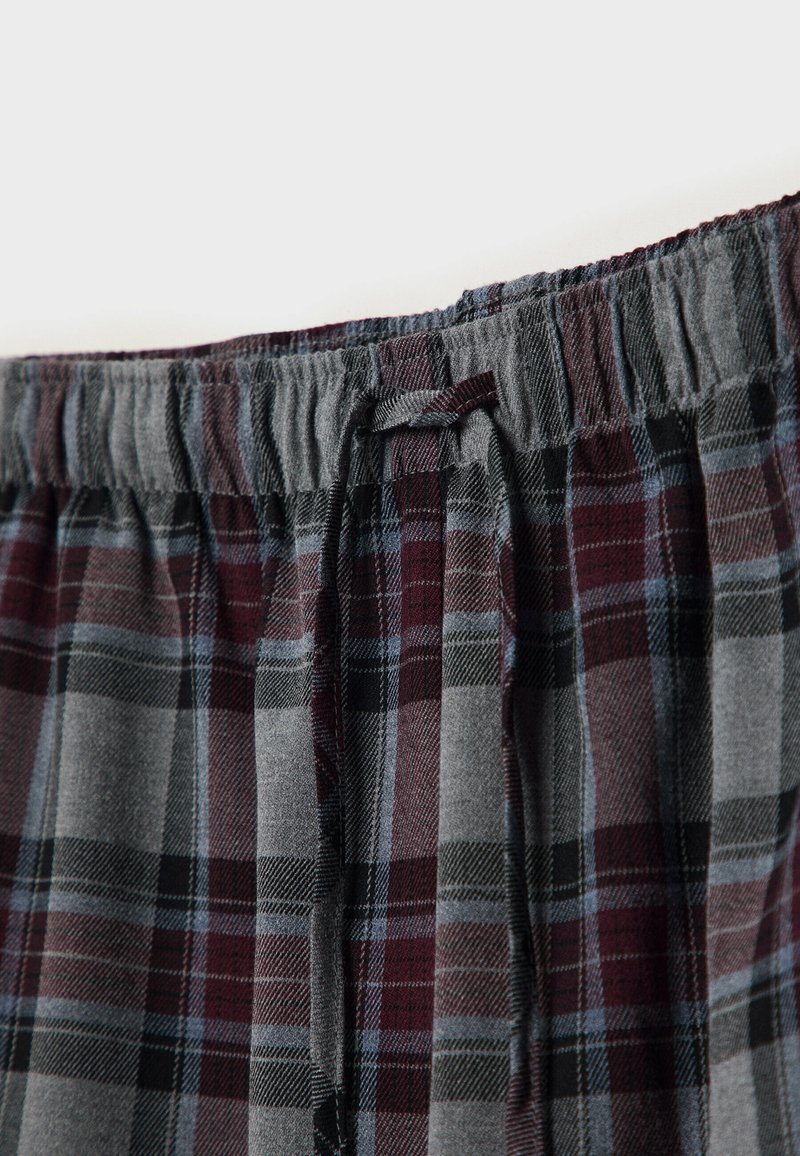 Spodnie w kratę z elastycznym pasem, w kolorach szarym, bordowym i czarnym. Miękki materiał z luźnym krojem i detalem w postaci sznurków.