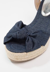 Vue de face d'une sandale compensée en tissu bleu marine avec un détail de nœud noué et une semelle plateforme en jute tressé.