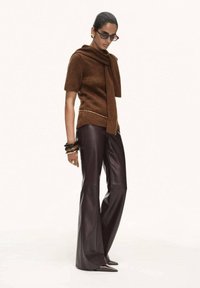 Brown short-sleeve sweater with a scarf detail, paired with high-waisted, wide-leg black leather pants. Black sunglasses and gold accessories.