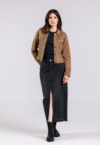 Veste en denim marron avec des boutons sur un haut côtelé noir, associée à une jupe en denim noire avec une fente sur le devant et des bottes noires à lacets.