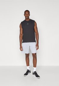 Débardeur de sport noir sans manches, short gris clair, chaussures de sport noires, chaussettes blanches, avec des détails de logo subtils sur les vêtements.