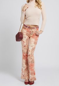 Dzwony w beżowym i koralowym wzorze patchworkowym z kwiatowymi i zwierzęcymi motywami; w zestawieniu z jasnym swetrem i bordowymi akcesoriami.