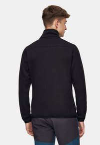 Czarna polarowa kurtka z wysokim kołnierzem, teksturowanym materiałem i minimalistycznym designem. Posiada bezszwowe ramiona i yoke pleców dla większego komfortu.