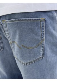 Jeans in denim azzurro chiaro con due tasche posteriori caratterizzate da cuciture gialle e un dettaglio di design curvo sui bordi delle tasche.