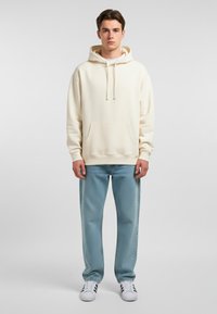 Felpa di colore crema realizzata in morbido tessuto, con tasca frontale e cordini. Abbinata a jeans azzurri chiari e sneakers bianche.