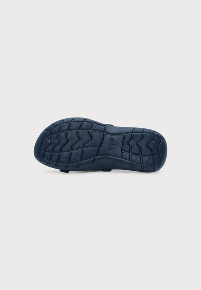 Semelle de chaussure bleu foncé avec motif de bande de roulement en zigzag et grille et nom de marque "Versace" embossé au centre.