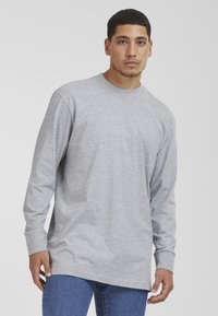 Camiseta de manga larga gris de tejido suave, con un escote redondo y un corte holgado. Combinada con jeans de mezclilla azul.