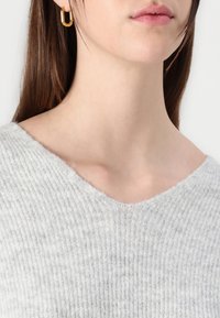 Maglione a coste grigio chiaro con scollo a V, che mette in risalto una texture morbida. Un orecchino a cerchio dorato aggiunge un dettaglio di contrasto.