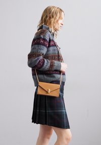 Pulover tricotat gri cu modele roșii și albastre, asortat cu o fustă plisată din tartan negru și o geantă de umăr din piele bej cu accesorii aurii.