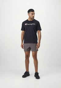 Melnā īsroka Champion T-krekls ar baltu logotipu, kopā ar pelēkiem šortiem un melniem sporta apaviem. Vienkāršs dizains ar brīvu piegriezumu.