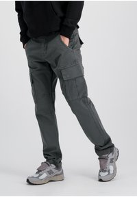 Gray cargo pants with multiple pockets, relaxed fit, slight sheen, and stitched detailing. Paired with gray sneakers.