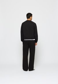 Fekete, hosszúujjú pulóver, cropped fazonnal, amely széles szárú nadrággal van párosítva. Az anyag puhanak és textúráltak tűnik.