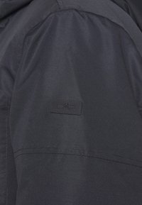 Mörk marinblå jacka med ett slätt, lättviktsmaterial. Har en svart CMP-logotyp på ärmen och en strukturerad, skräddarsydd design.