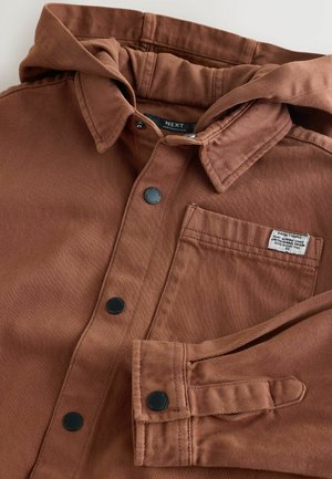 Rudas, užsegamas švarkas su kapuce. Yra juodi spaudimo mygtukai ir krūtinės kišenė. Tekstūruota medžiaga su matomomis siuvimo detalėmis.