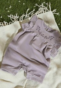 Romper di cotone lilla con dettagli in pizzo sulle spalle, motivo floreale ricamato sul petto e chiusura a pressione sul fondo. Disposto su un tessuto testurizzato.