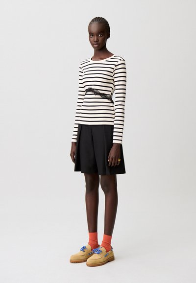 Top de manga larga a rayas negras y crema con detalle de encaje, combinado con una falda negra, calcetines naranjas y zapatos beige con cordones azules.