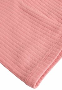 Gros plan d’un tissu côtelé rose doux avec des lignes horizontales de tricot visibles et un bord d’ourlet soigneusement cousu.