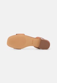 Sandale beige avec une tige lisse, un design à bout ouvert, et une semelle en caoutchouc avec une prise texturée. Marquée avec la marque "ALDO".
