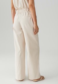 Lange broek in lichtbeige stof, met een elastische tailleband en twee achterzakken. Gladde textuur met een strak ontwerp.