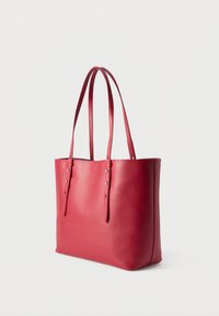 Κόκκινη δερμάτινη τσάντα tote με δύο μακριά ρυθμιζόμενα λουριά ώμου και λεία επιφάνεια, εμφανιζόμενη σε απλό ανοιχτό φόντο.