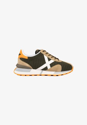 Zapatilla ligera con malla verde oscuro, superposiciones de ante beige, X blanco lateral y detalles naranjas en el talón y la suela.