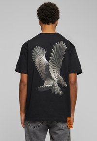 Sort bomuld T-shirt med et stort, detaljeret ørne grafik på ryggen, der viser intrikate fjer mønstre og en dynamisk pose.