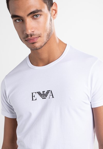 Bela bombažna majica s krožnim ovratnikom, kratkimi rokavi in črnim logotipom "EVA" s krilnimi poudarki natisnjenim na prsih.