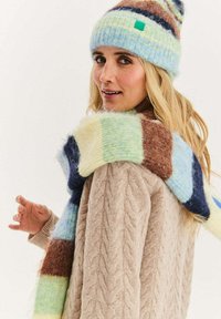 Zestaw z dzianym kapeluszem i szalikiem w pastelowych odcieniach niebieskiego, zielonego i brązowego; miękka tekstura, wzór w paski, na kapeluszu znajduje się mała zielona etykieta.