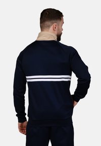 Marineblauer Pullover mit beigem Kragen, der über die Rückseite weiße Streifen aufweist. Hergestellt aus glattem Stoff mit einer legeren Passform und gerippten Bündchen.