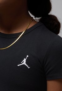 Fekete, kerek nyakú póló, bal mellrészen fehér hímzett Jordan logóval, arany színű fém lánc nyaklánccal.