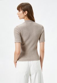 Top de manga corta, de canalé en beige con diseño de cuello alto; presenta puños enrollados y una silueta ajustada. Adecuado para uso casual.