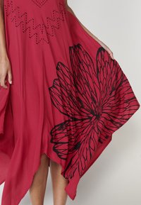 Rotes Kleid aus leichtem Stoff mit fließendem Design. Besitzt großen schwarzen Blumenprint und ausgeschnittene Sternmuster im Oberteil.