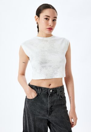 Top corto blanco con un acabado texturizado, que presenta mangas cortas y un escote alto. Combinado con pantalones de mezclilla negros de tiro alto.