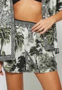 I pantaloni corti in un tessuto leggero presentano una stampa di tigri in bianco e nero e palme, con un elastico in vita arricciato e un motivo leopardato in accent.