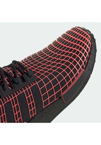 Černé tenisky s červeným mřížkovým vzorem, textilním svrškem, černými tkaničkami a černou podrážkou s bočním akcentem značky.