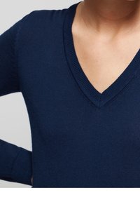 Pull col en V bleu marine avec texture côtelée et poignets côtelés. Coupe ajustée, tissu doux et détails de couture minimalistes pour une finition nette.