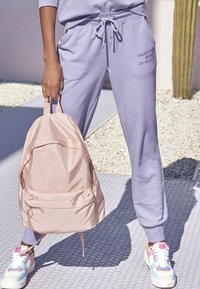 Lichtpaarse sweatpants met zakken, gecombineerd met een blushroze rugzak en multikleurige sneakers. De outfit heeft een relaxte pasvorm en trekkoorden.